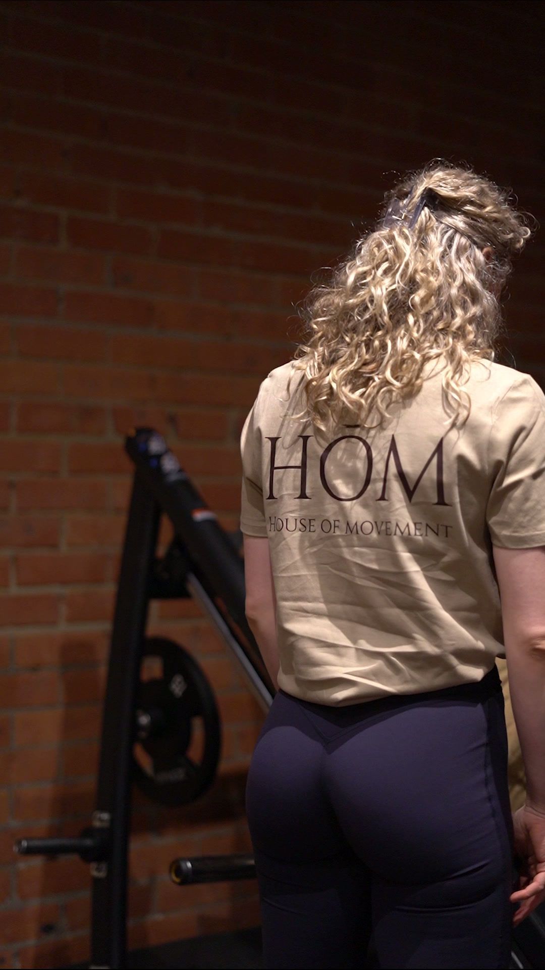 Een lid in een HŌM-shirt tegen de bakstenen muur van de zaal